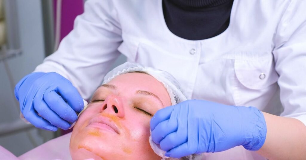 A person receives a facial treatment personalized for their skin type while lying down; the clinician, wearing gloves and a white coat, discusses the best options such as chemical peels.