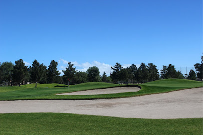 A golf course with a sand bunker in the foreground, green grass, scattered trees, and a clear blue sky.